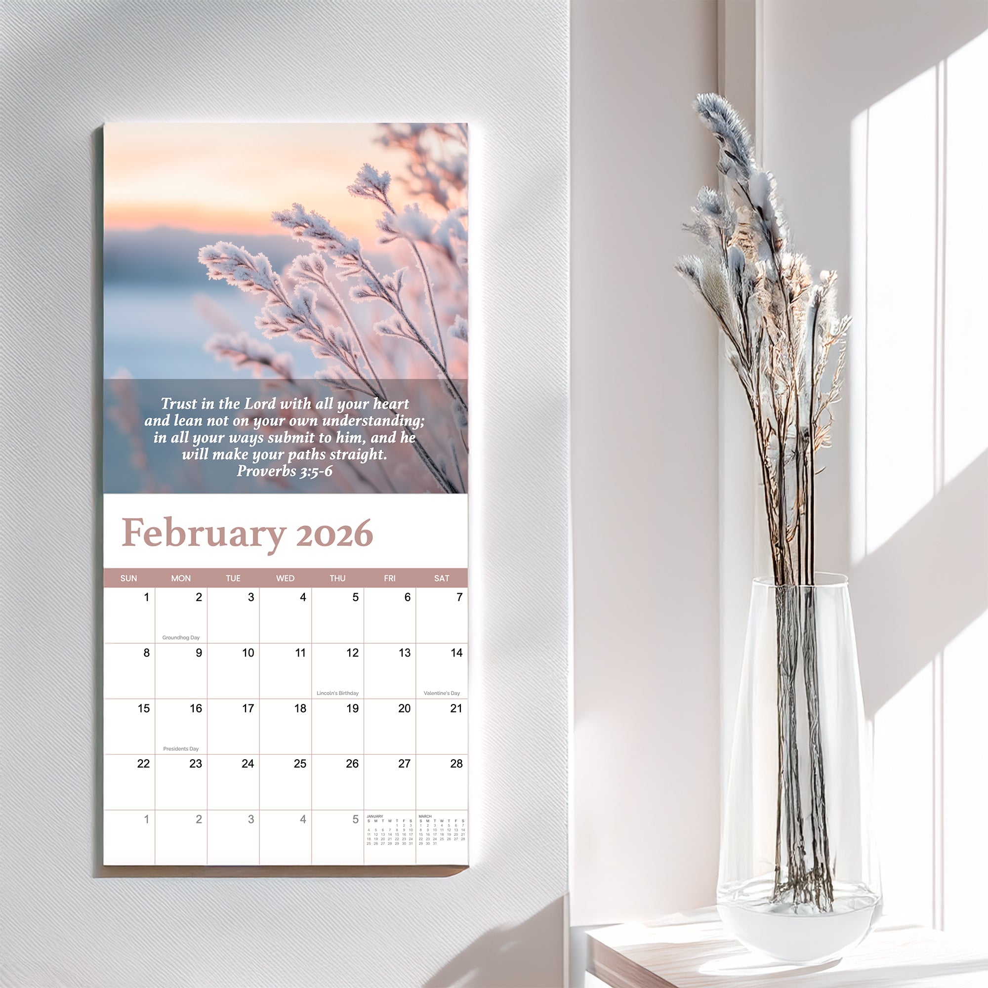 The 2026 Religious Wall Calendar by HannahFaithstore displays Proverbs 3:5-6 for February, featuring frosted plants and dried flowers in a clear vase on a white table—a thoughtful faith-based gift.