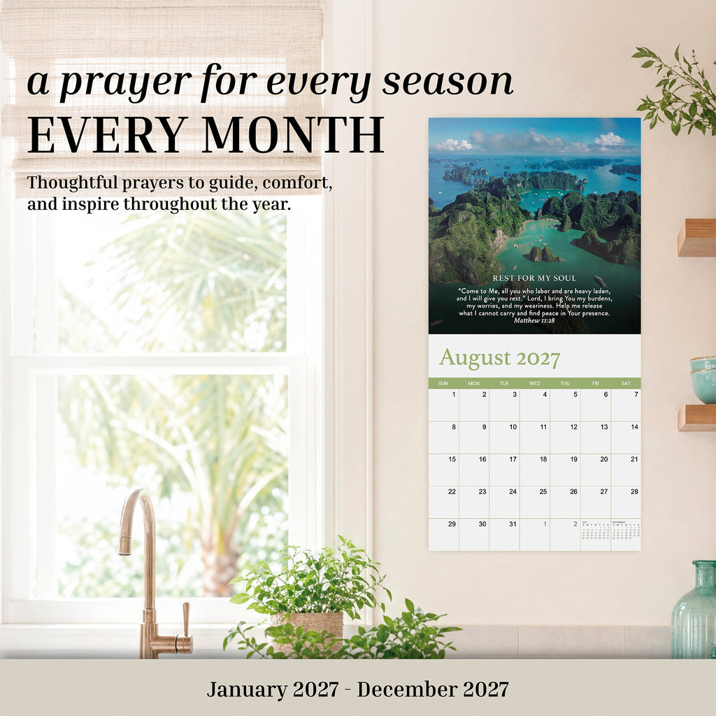 The 2027 Prayer Wall Calendar by HannahFaithstore is a faith-based calendar featuring monthly prayers and inspiring nature photography. The August page highlights tropical scenery, making it a thoughtful Bible verse calendar gift—perfectly displayed above your desk with plant decor on a beige wall.