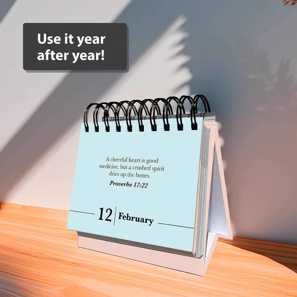 The HannahFaithstore Religious Perpetual Calendar displays a Bible verse for February 12. "Use it year after year!" appears above, as sunlight and a plant cast shadows on the wooden surface.